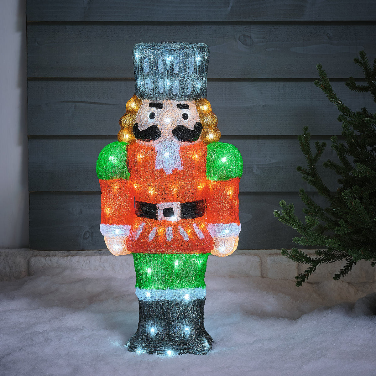 Einzelner beleuchteter LED-Nussknacker aus Acryl mit roter Jacke und grünem Hosenbein im Schnee