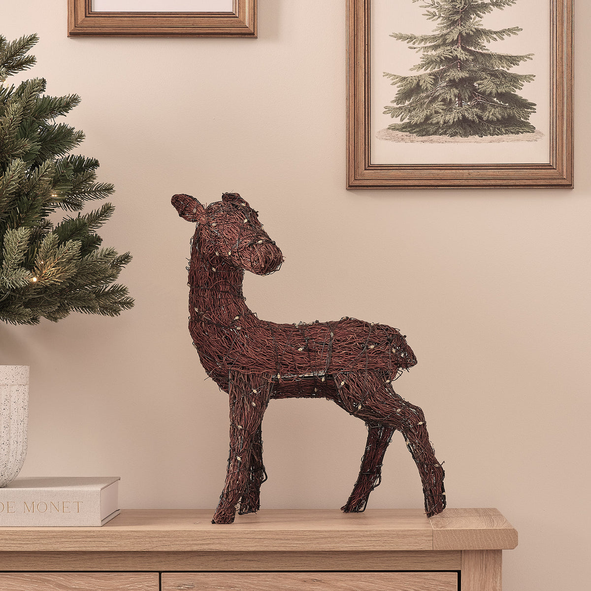 LED-Rentier aus Zweigen ohne Beleuchtung auf Sideboard neben Weihnachtsbaum und Bilderrahmen