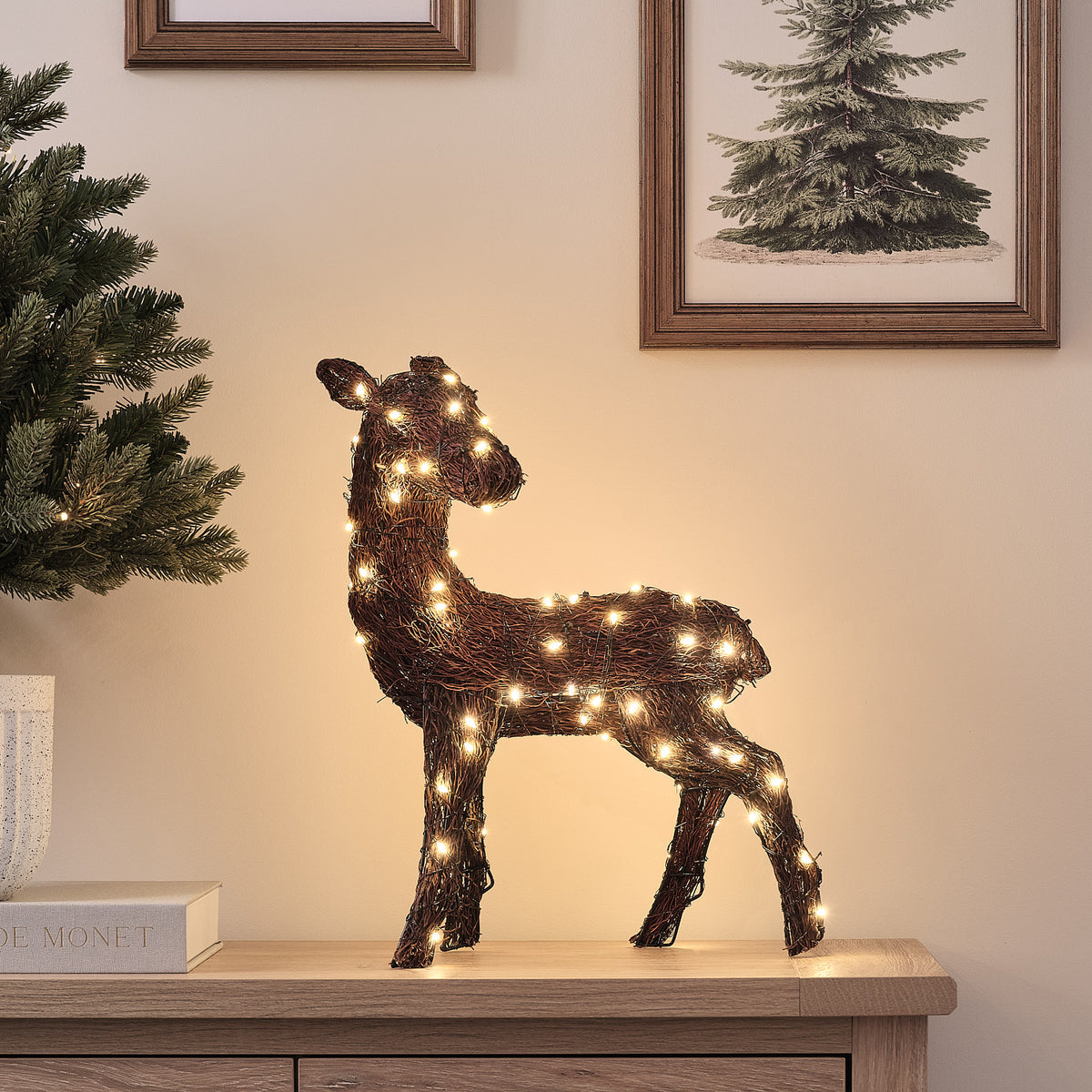 LED-Rentier aus Naturzweigen mit eingeschaltetem warmweißem Licht auf Sideboard vor Wand