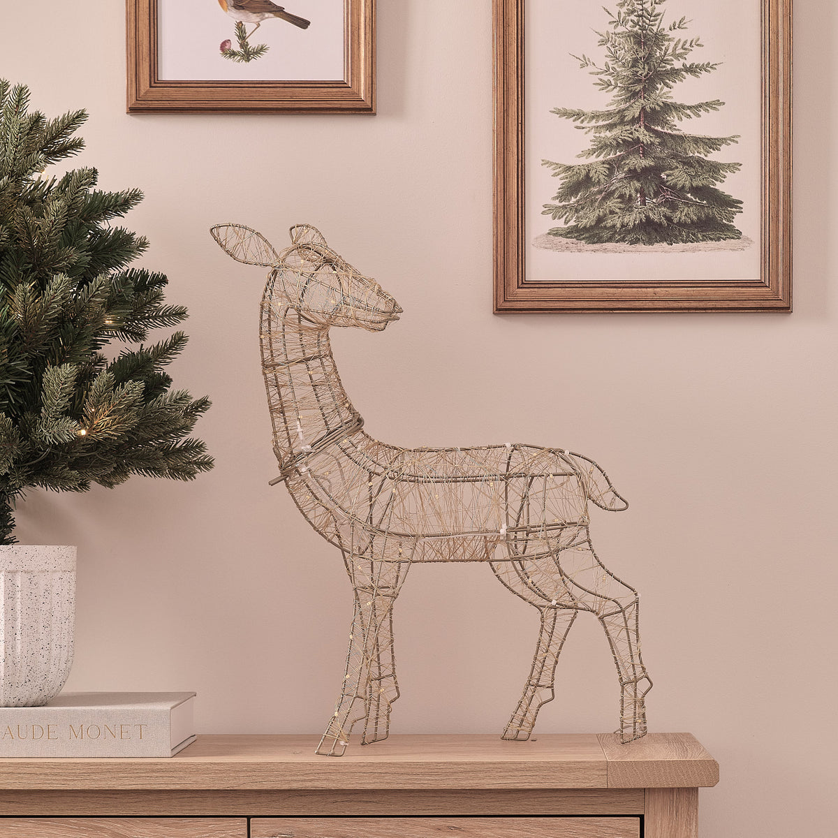 Goldene LED-Rentier-Hirschkuh mit kaltem Weißlicht auf Sideboard vor Wand mit Bildern