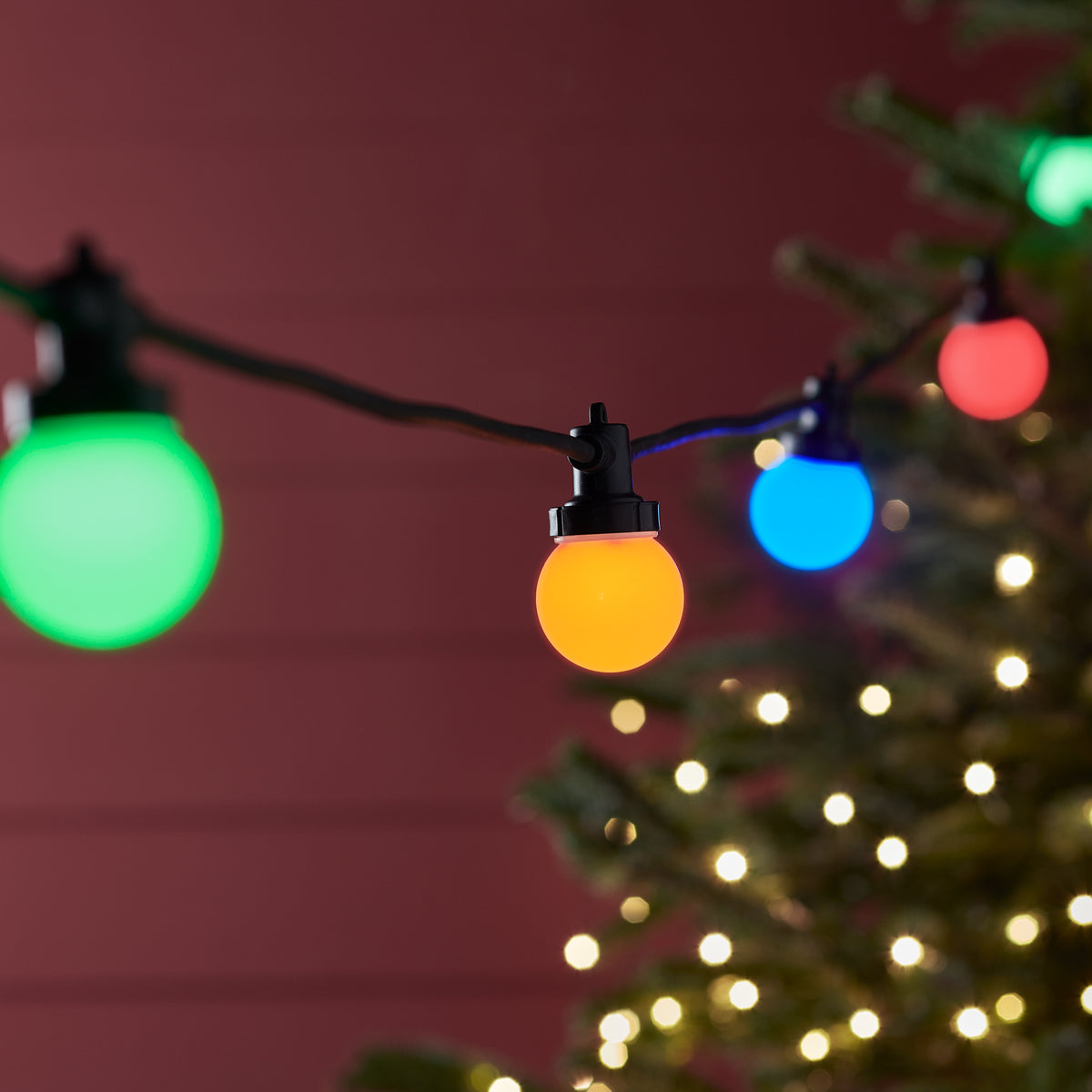 Bunte LED-Glühbirnen an schwarzem Kabel vor rotem Hintergrund bei Nacht
