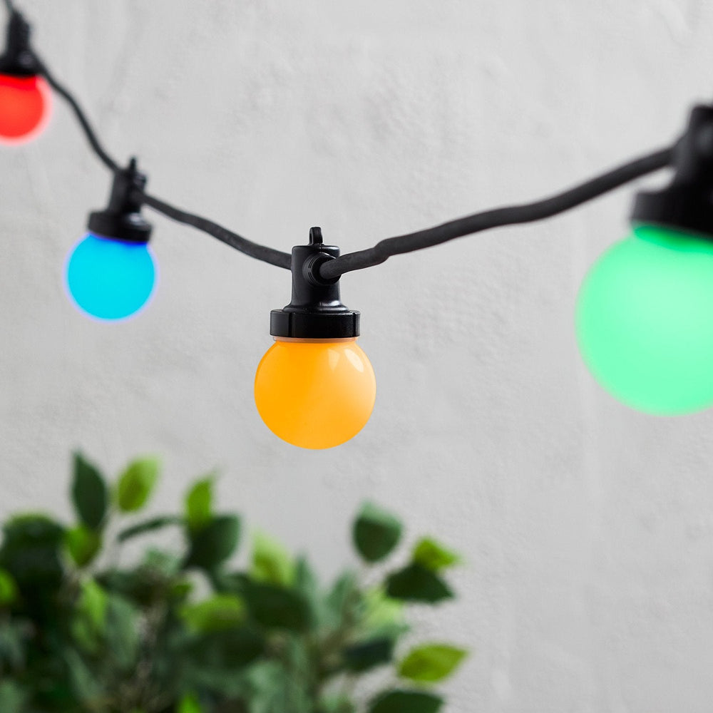 Nahaufnahme bunte LED-Glühbirnen an schwarzem Kabel vor weißer Wand