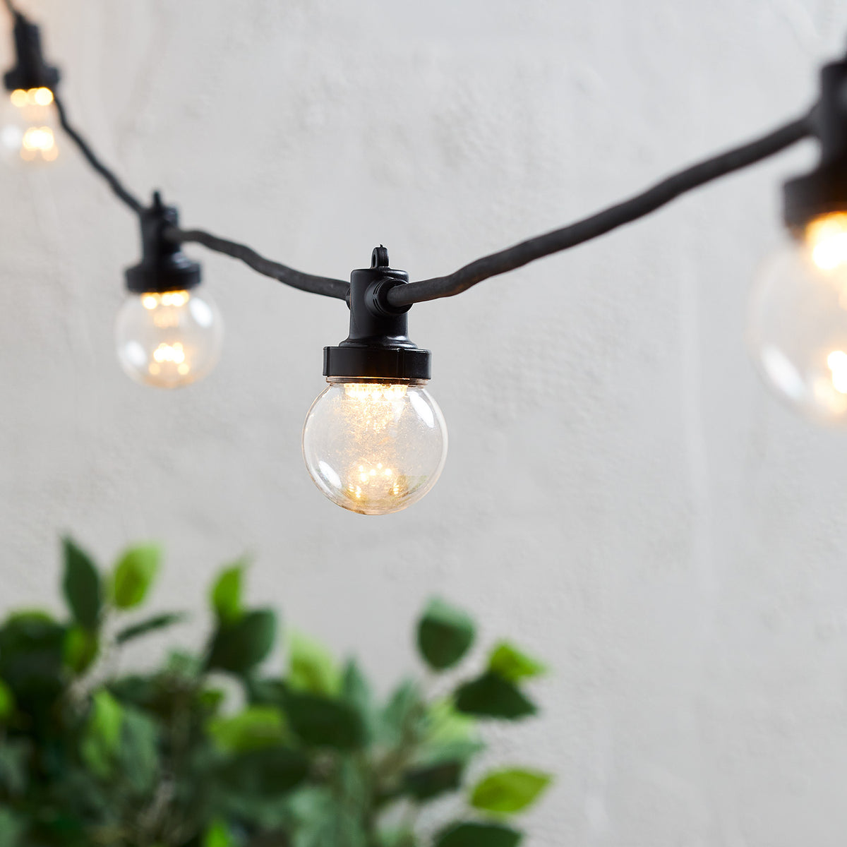 Nahaufnahme einer warmweißen LED-Glühbirne an schwarzer Party-Lichterkette vor weißer Wand
