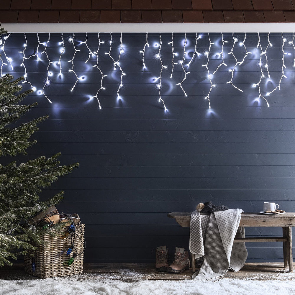 Lange weiße LED Eiszapfen Lichterkette an dunkler Wand mit Bank, Decke und Winterstiefeln