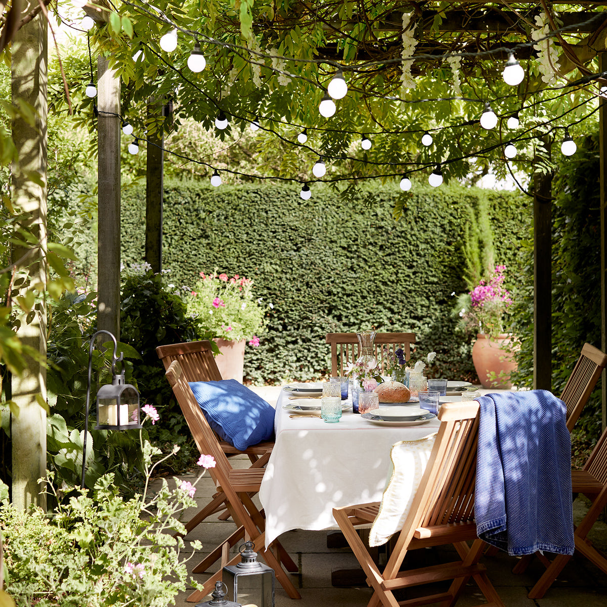 Pro Connect Lichterkette hängt dekorativ unter einem grünen Pergola-Dach über gedecktem Gartentisch