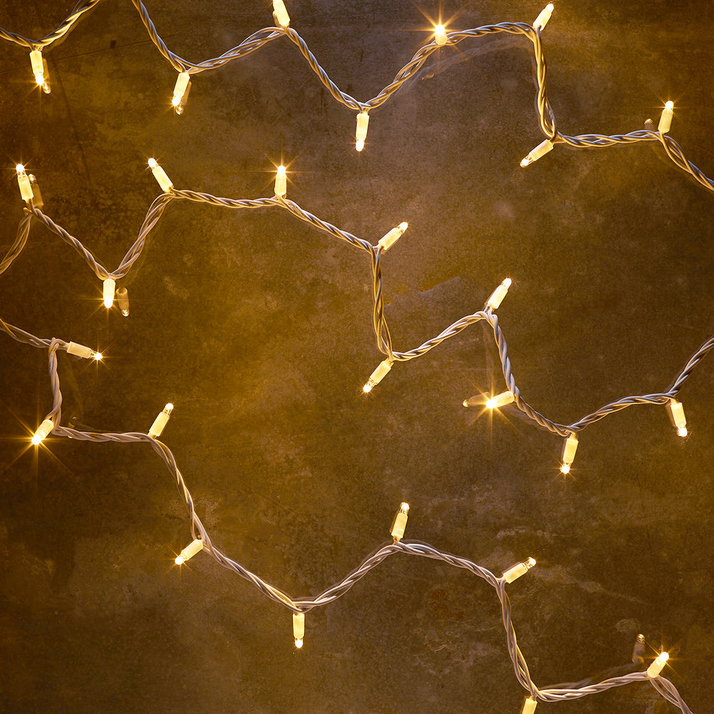 Warmweiße LED-Lichterkette mit weißem Kabel auf dunklem Untergrund leuchtend