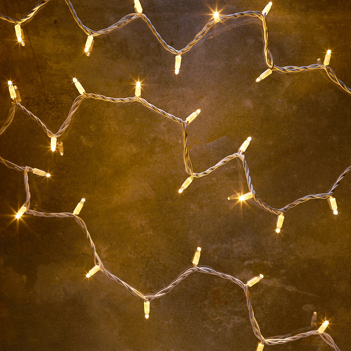Warmweiße LED-Lichterkette mit weißem Kabel auf dunklem Untergrund leuchtend