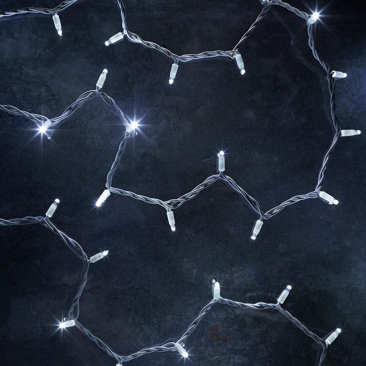 Nahaufnahme einer weißen LED-Lichterkette mit weißem Kabel auf dunklem Untergrund