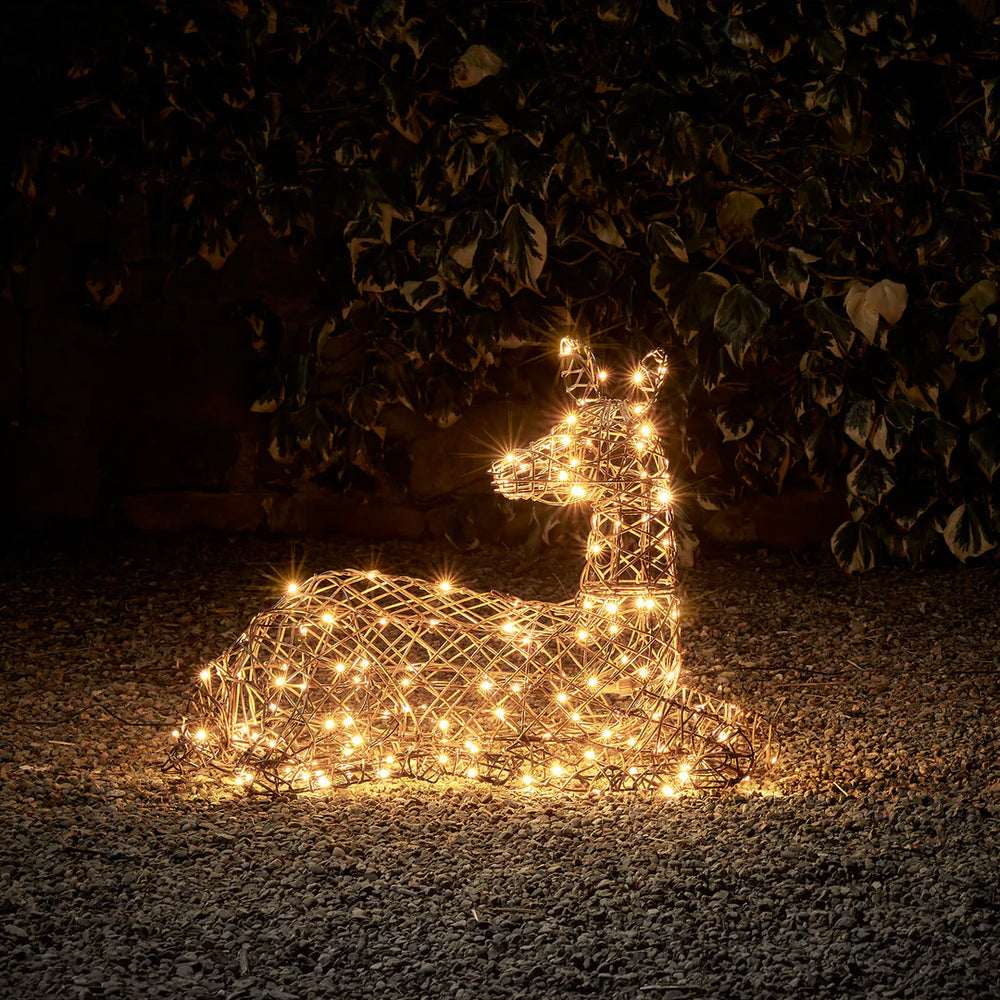 Liegendes LED-Rentier in brauner Rattanoptik mit warmweißen Lichtern bei Nacht im Garten