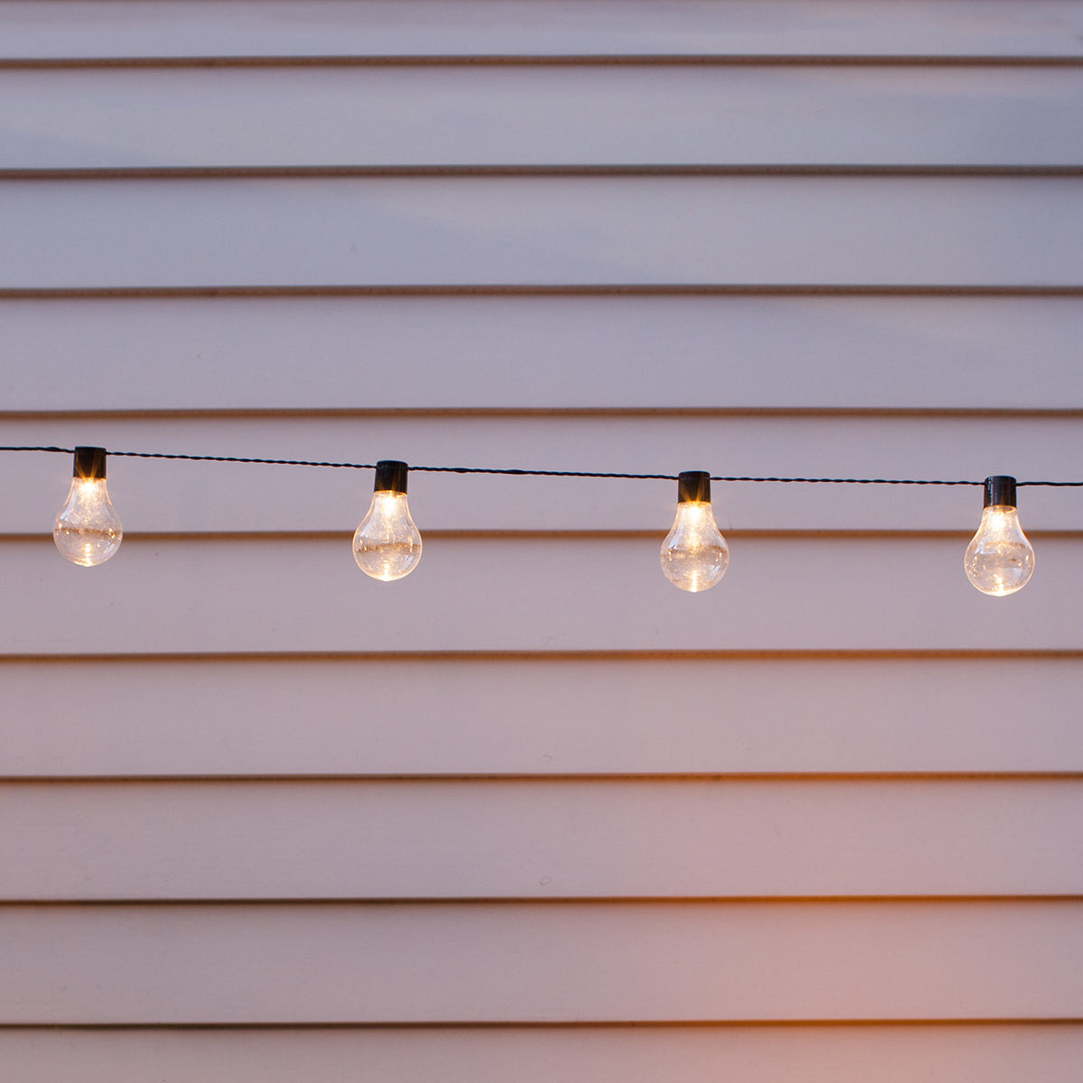 Nahaufnahme der warmweißen LED-Kugeln der Solar Party Lichterkette vor weißer Wand