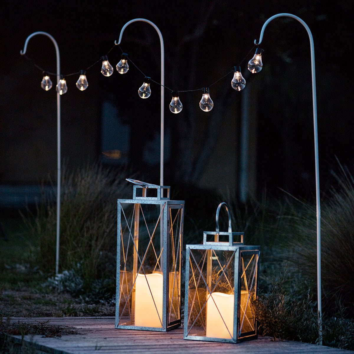 Solar Lichterkette mit warmweißen LEDs über zwei Metallstäben und leuchtende Laternen am Boden