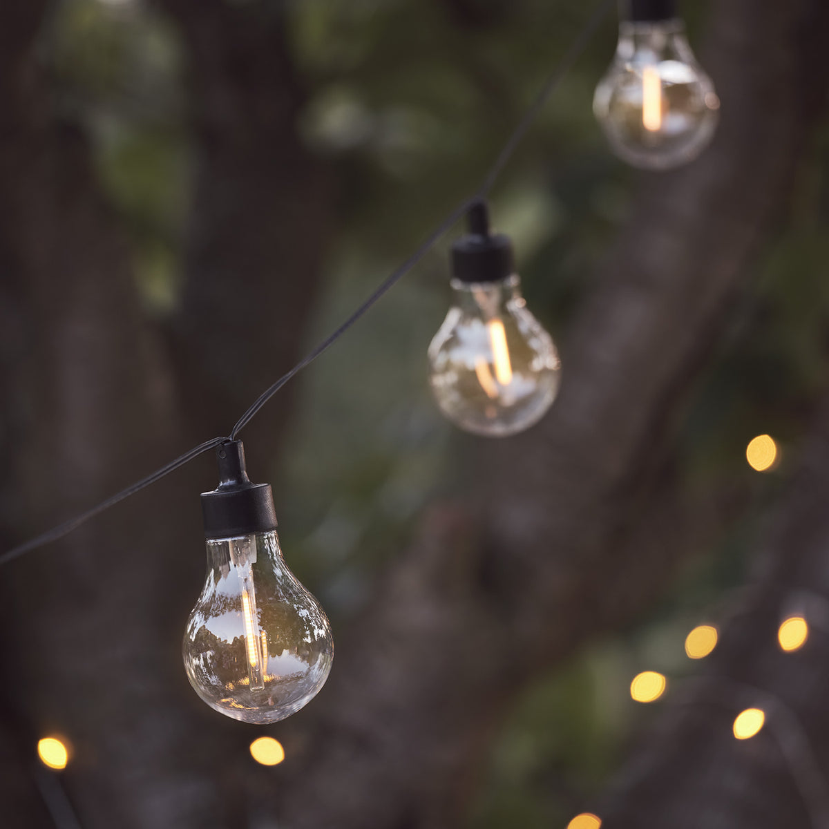Warmweiße LED-Glühbirnen an schwarzem Kabel vor unscharfem Hintergrund mit Lichterglanz