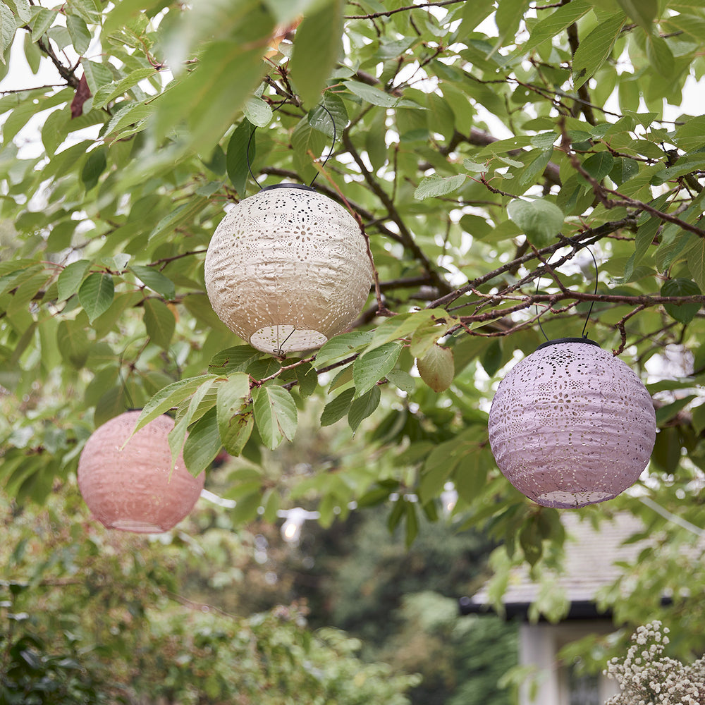 Drei pastellfarbene Tyvek Solar Lampions in Rosa, Weiß und Lila hängen an einem grünen Baum