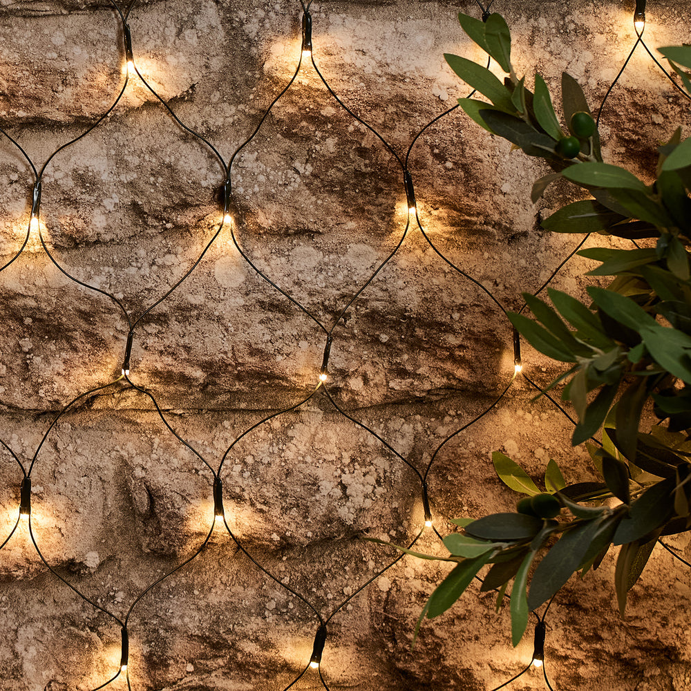 Solar Lichternetz mit warmweißen LEDs an einer Steinwand mit grünen Blättern