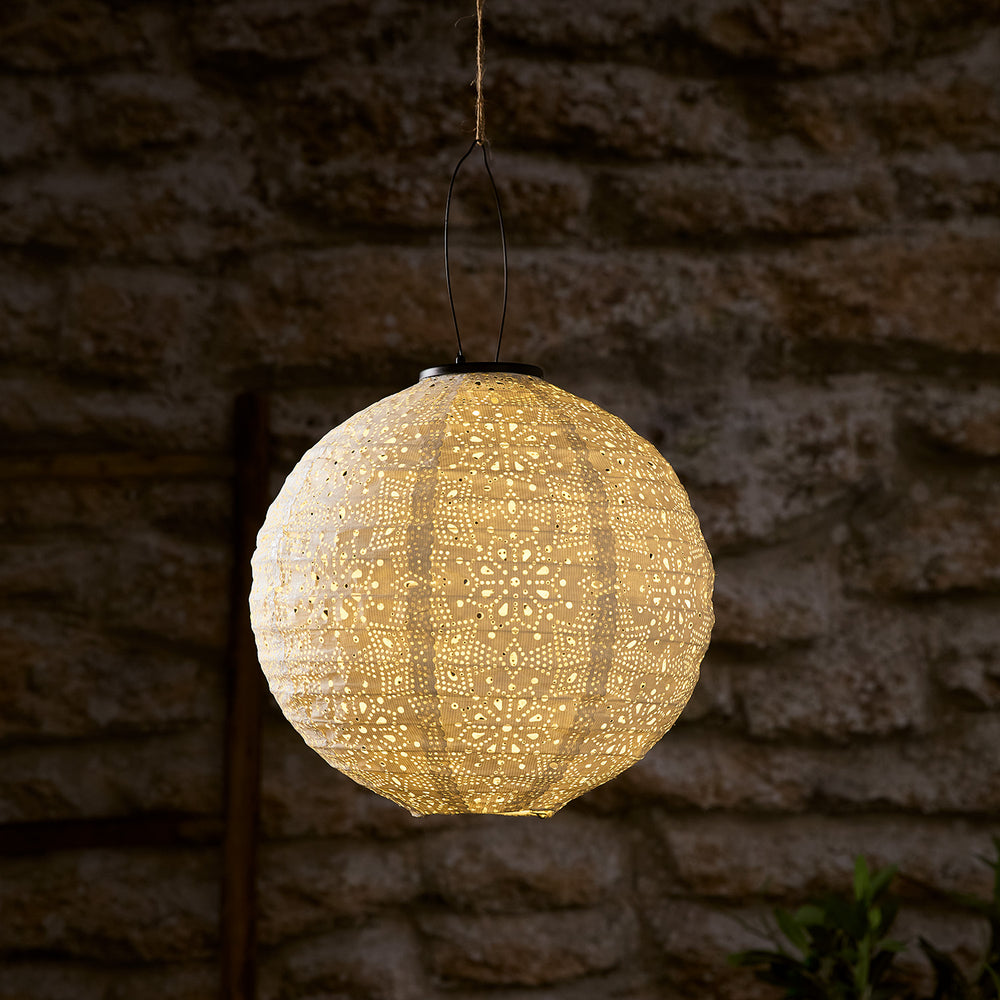 Leuchtender weißer Tyvek Solar Lampion mit floralem Muster vor dunkler Steinwand