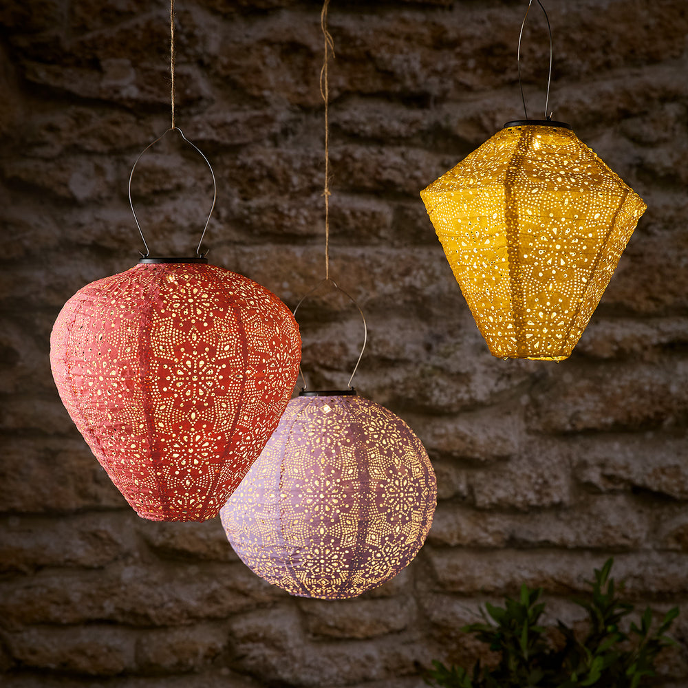 Drei bunte Tyvek Solar-Lampion mit Blumenmuster leuchtend vor Steinwand