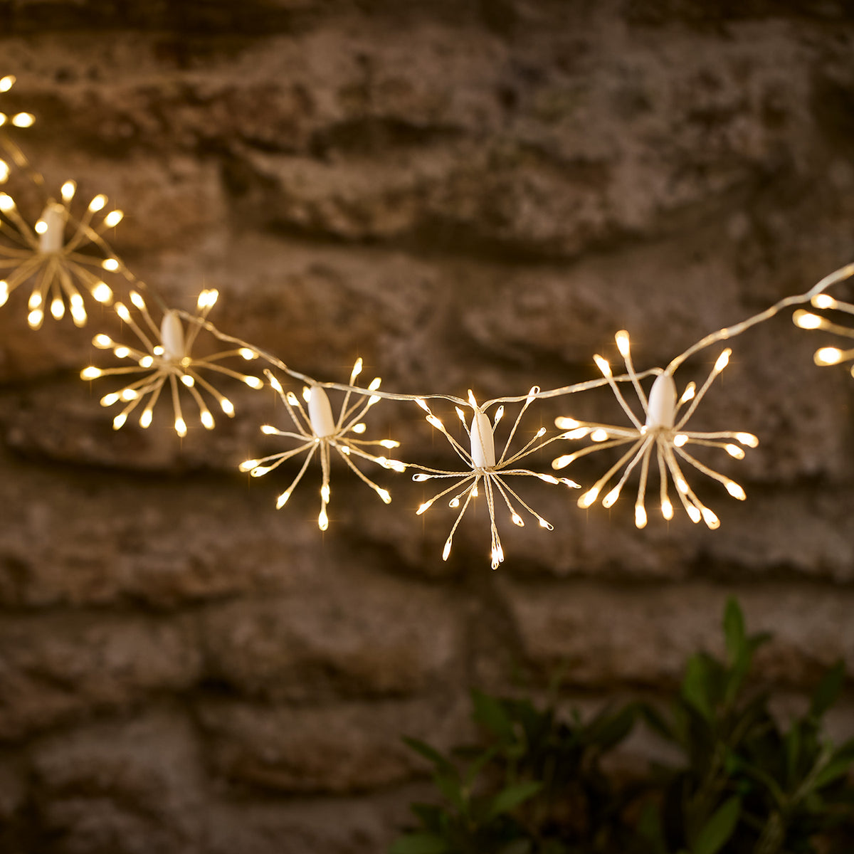 Leuchtende Starburst LED Lichterkette mit warmweißem Licht vor einer Steinwand