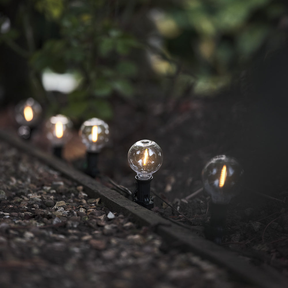 Solarbetriebene LED-Lichterkette mit leuchtenden Glaskugeln am Boden im Garten