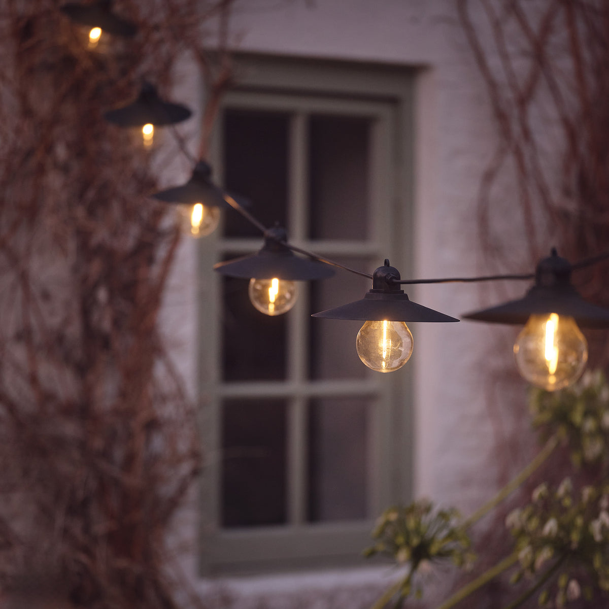 Solarbetriebene Lichterkette mit mehreren warmweißen LED-Glühbirnen vor einem Fenster im Außenbereich