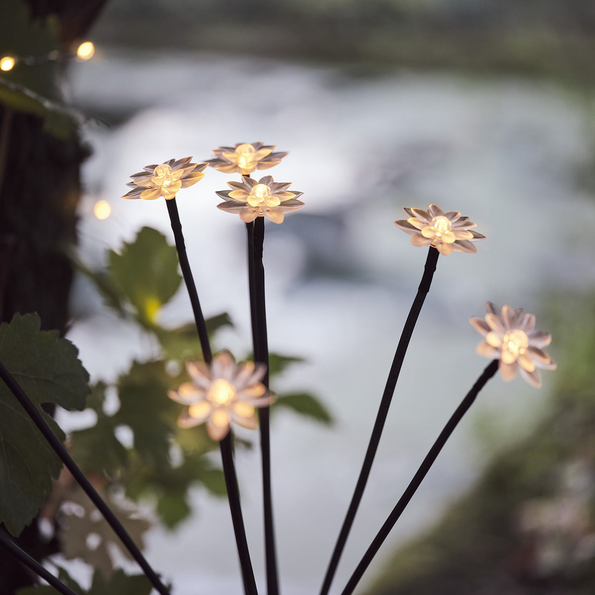 Detailansicht von mehreren leuchtenden Solar-Blumen auf schwarzen Stangen vor unscharfem Hintergrund