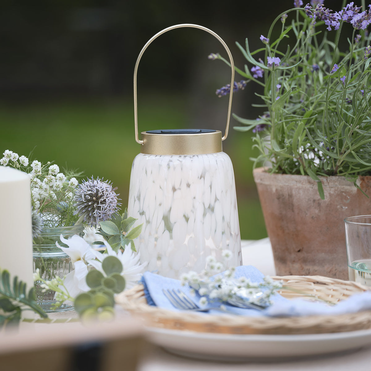 Solarlaterne auf gedecktem Tisch mit Blumen und goldfarbenem Deckel im Außenbereich