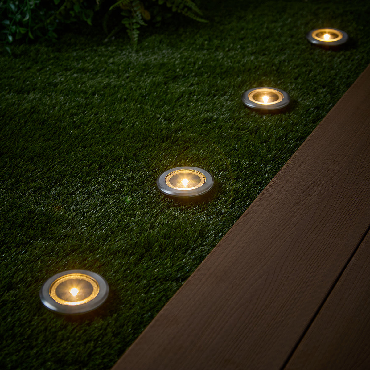 Drei Solar-Spots mit warmweißem Licht in Rasen neben Holzterrasse