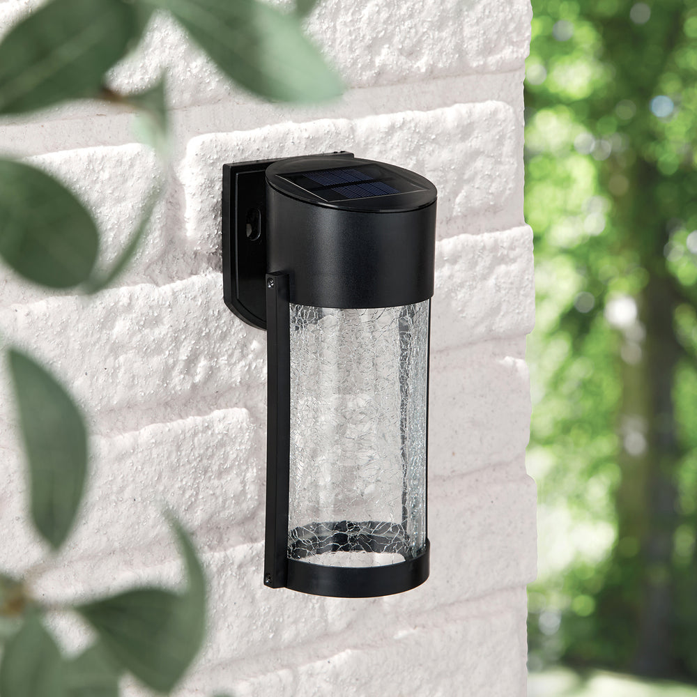 Solar-Wandleuchte mit gecrackeltem Glaszylinder an weißer Außenwand bei Tageslicht