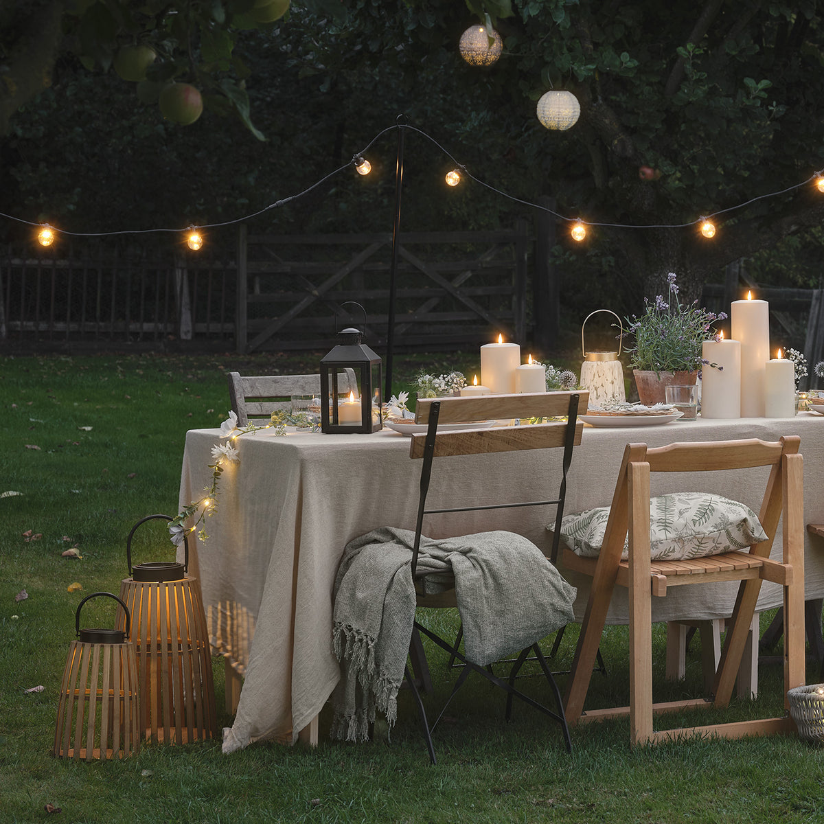 Gartenparty mit gedecktem Tisch, Kerzen und Bambus-Solarlaterne auf Rasen bei Dämmerung