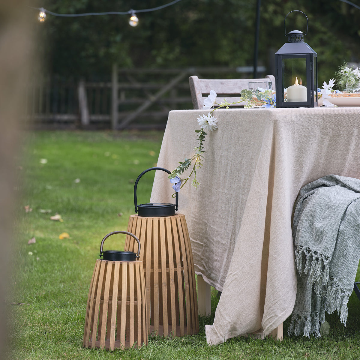 Große und kleine Bambus-Solarlaterne neben gedecktem Gartentisch mit Tischdecke