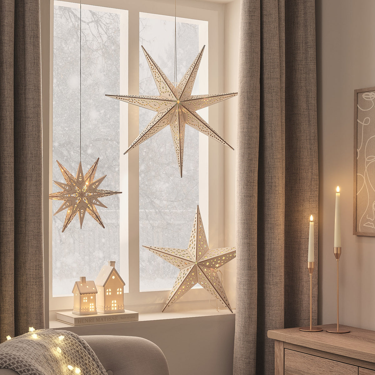Drei verschiedene Sterne aus Holz mit LED-Beleuchtung hängen vor Fenster mit winterlicher Kulisse