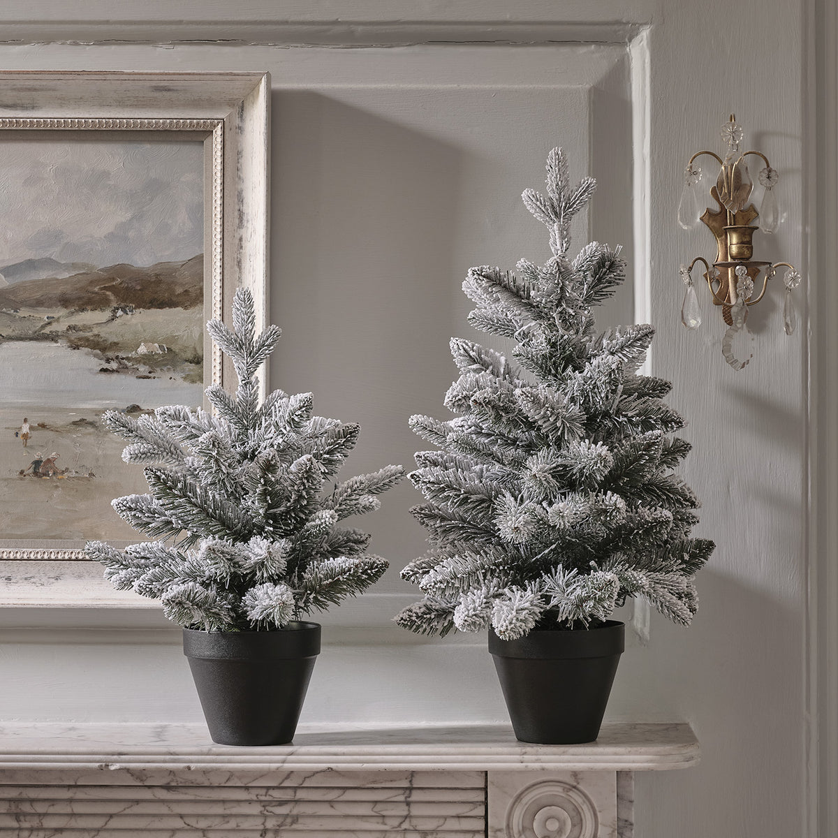 Nahaufnahme von zwei verschneiten Weihnachtsbäumen mit warmweißen LEDs in schwarzen Töpfen