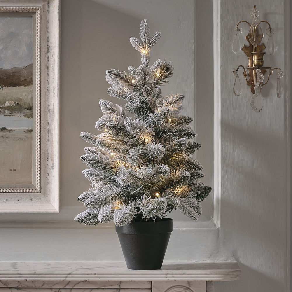 60 cm hoher verschneiter LED-Weihnachtsbaum in schwarzem Topf auf Marmorplatte vor grauer Wand