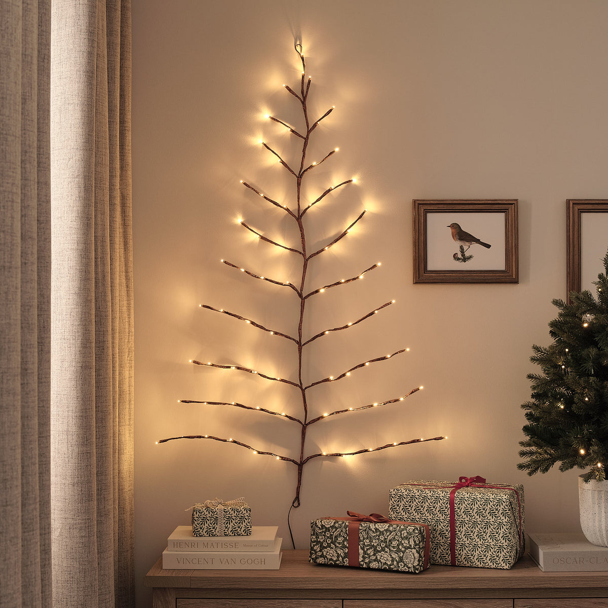 Goldener LED-Wandbaum mit warmweißen Lichtern an Wohnzimmerwand neben Bildern und Geschenken