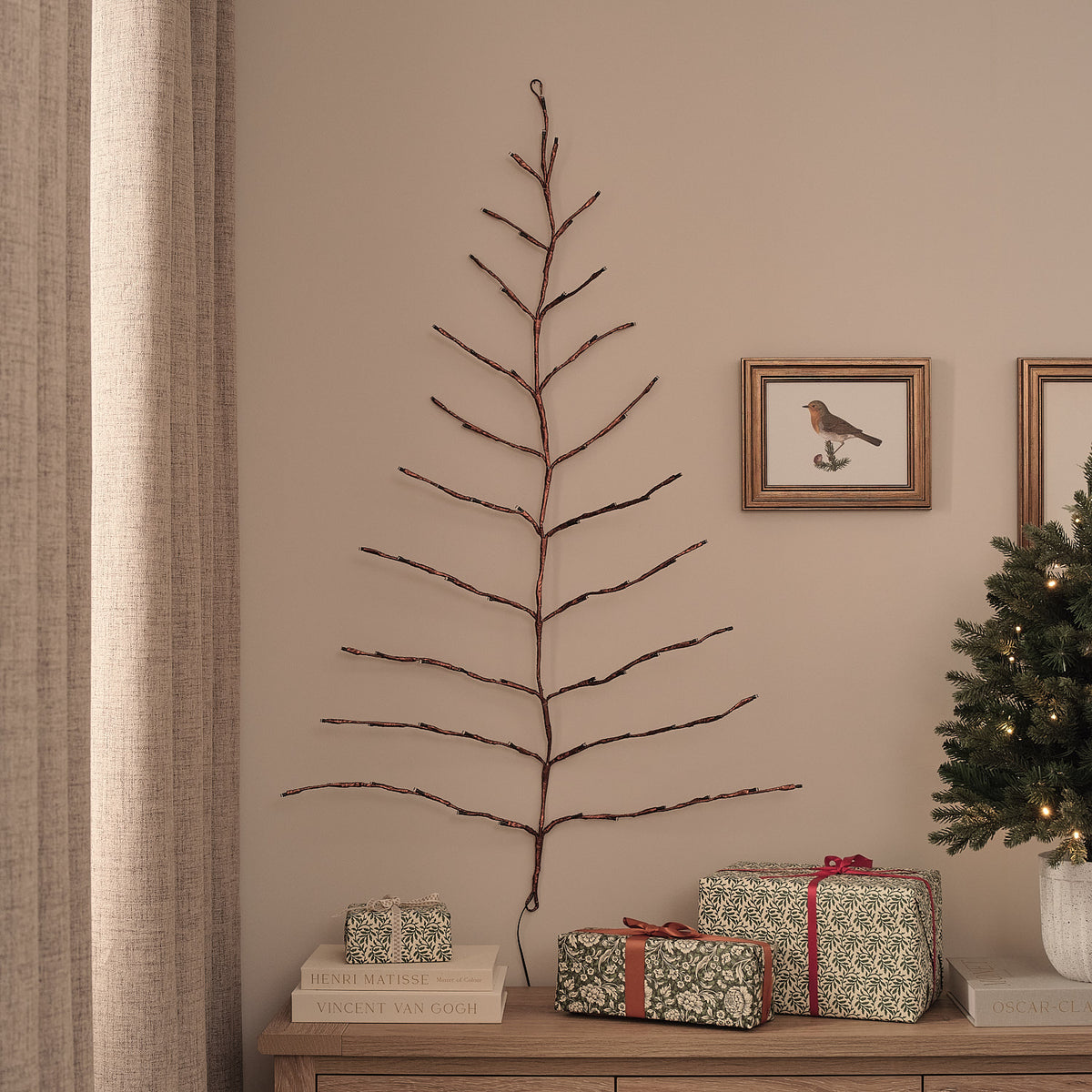 Unbeleuchteter goldener LED-Wandbaum an Wohnzimmerwand neben Weihnachtsbaum und Geschenken
