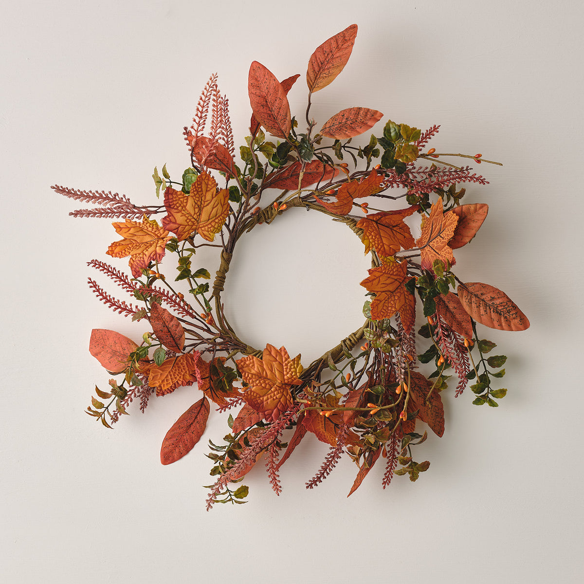 Herbstkranz mit orangefarbenen Ahornblättern und roten Gräsern vor weißem Hintergrund