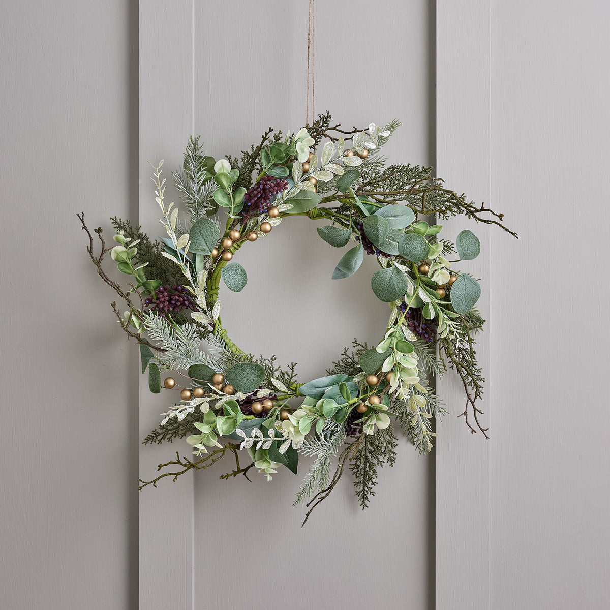 Weihnachtskranz mit grünen Blättern, goldenen Beeren und Zweigen an grauer Wand hängend