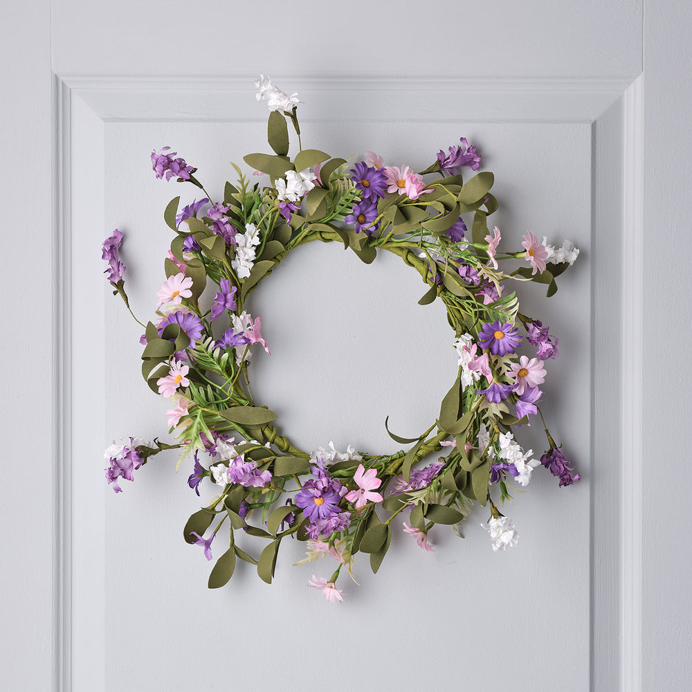 Frühlingskranz mit lila, rosa und weißen Wildblumen und grünem Kunstlaub an weißer Tür