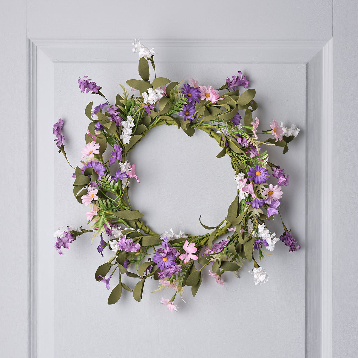 Frühlingskranz mit lila, rosa und weißen Wildblumen und grünem Kunstlaub an weißer Tür