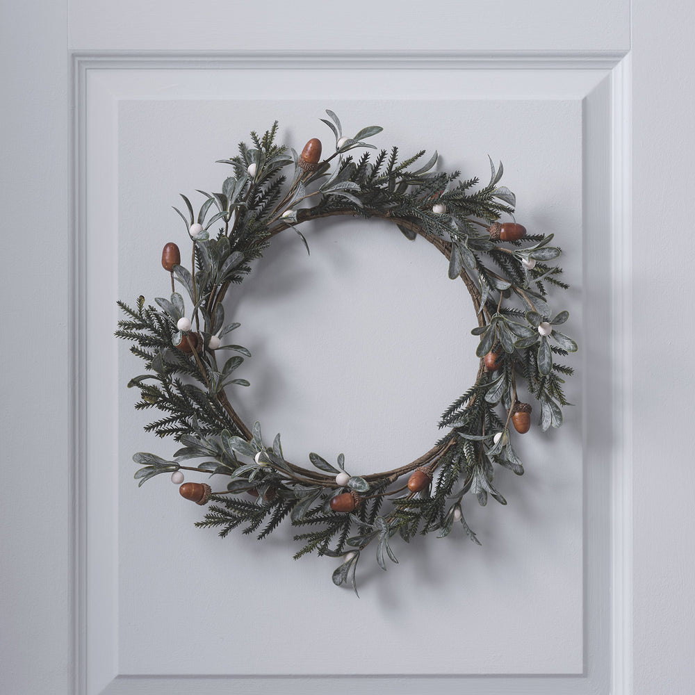 Weihnachtskranz mit Eicheln und weißen Beeren an weißer Tür hängend