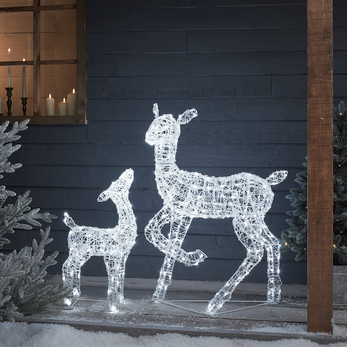 Solar-LED-Rentiere Hirschkuh und Rehkitz beleuchtet vor dunkler Holzfassade mit Kerzen