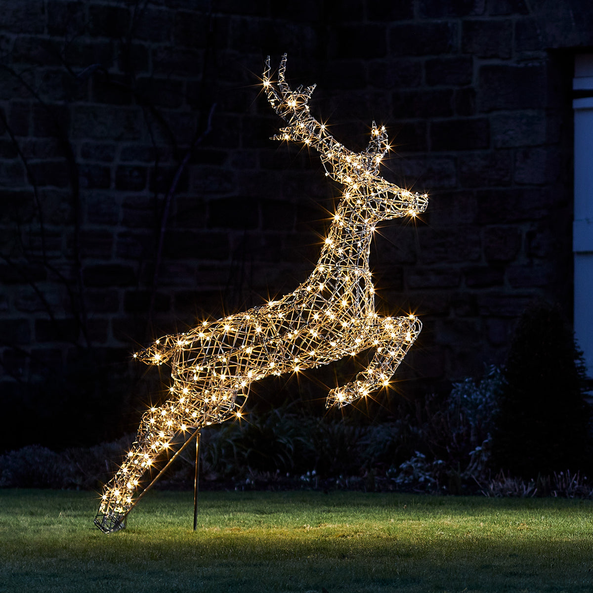 Springendes Rentier aus grauem Metall mit warmweißen LED-Lichtern beleuchtet bei Nacht