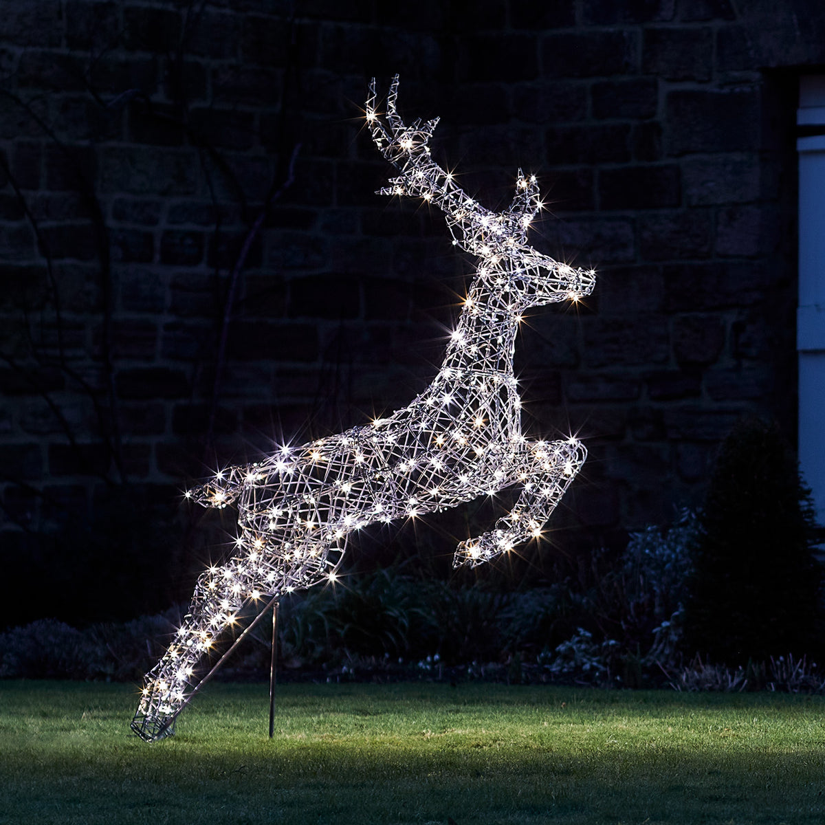 Springendes Rentier mit kühlen weißen LED-Lichtern beleuchtet auf Rasen bei Nacht