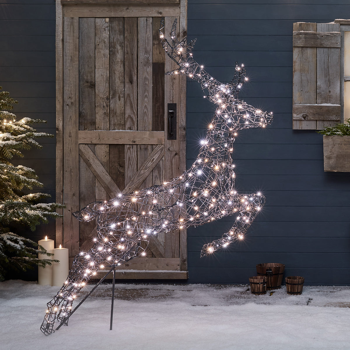 Springendes Rentier mit warmweißen LEDs beleuchtet auf verschneitem Boden vor Hauswand