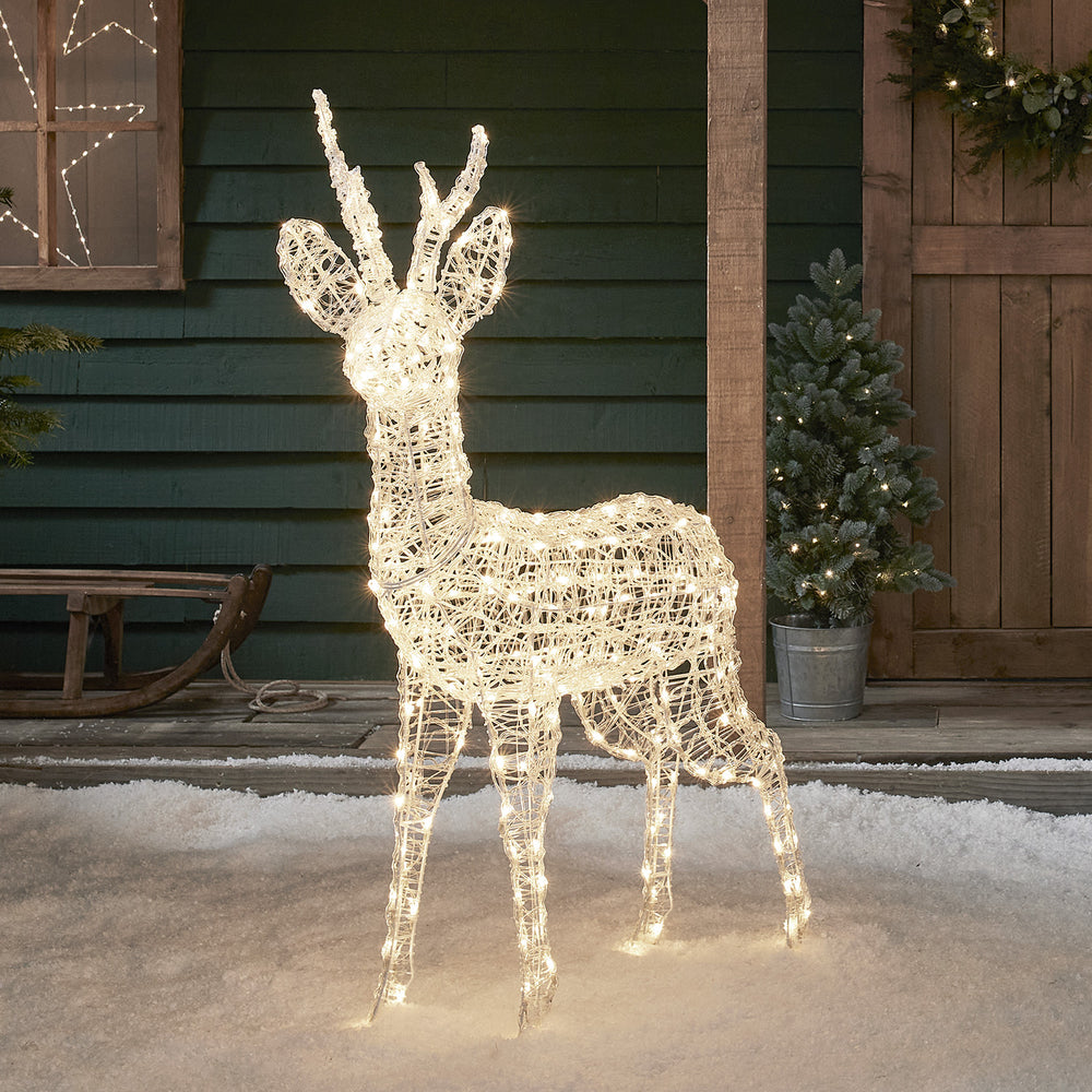 Beleuchtetes Acryl-Rentier mit warmweißen LEDs steht auf Schnee vor Hauswand