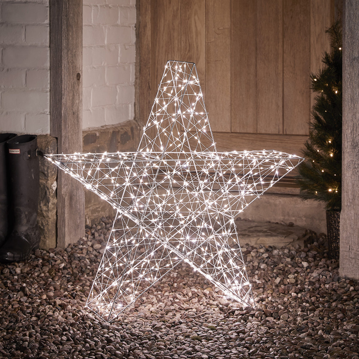 Großer 82cm hoher Bicolor LED Stern mit weiß leuchtenden LEDs auf Kiesboden vor Holztür