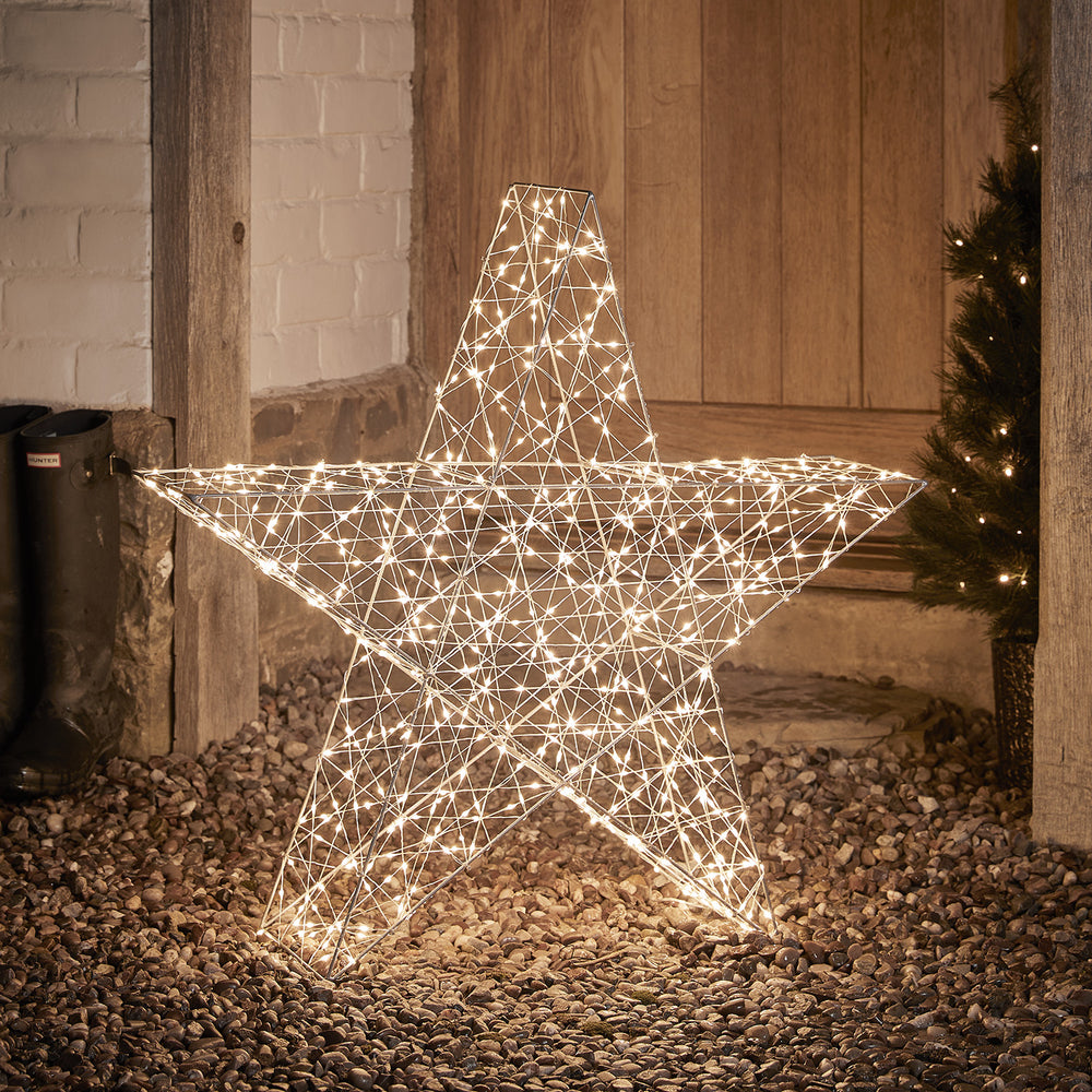 Großer 82cm hoher Bicolor LED Stern mit warmweiß leuchtenden LEDs auf Kiesboden vor Holztür
