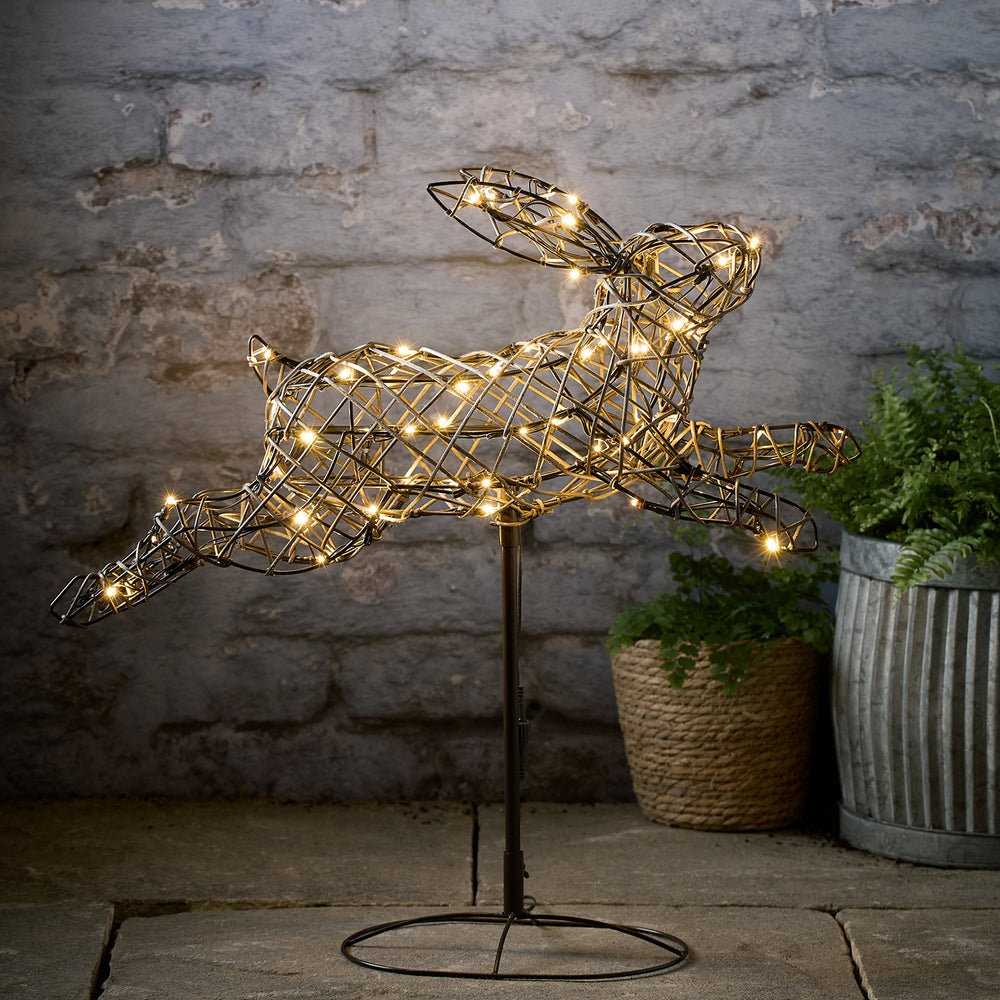 Leuchtende LED-Figur eines hüpfenden Hasen aus braunem Rattanimitat auf Metallständer