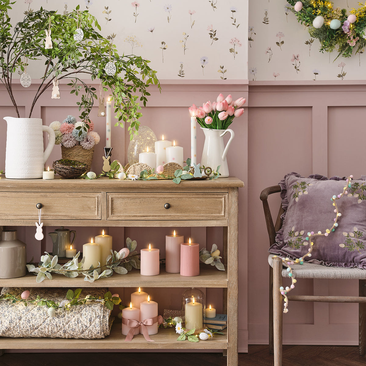 Osterdeko mit LED-Girlande, Kerzen, Blumen und Hasenfiguren auf Kommode und Stuhl