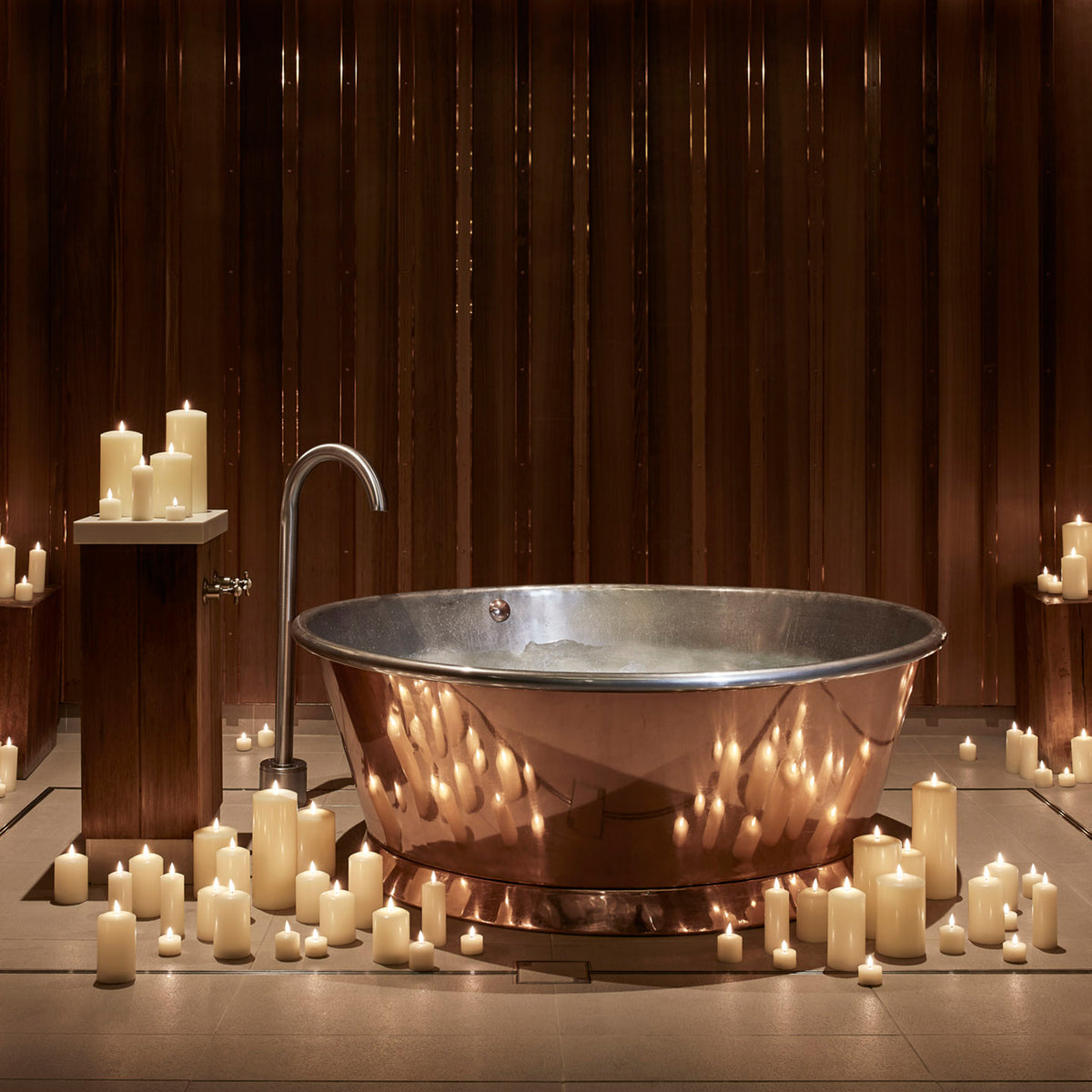 Kupferbadewanne umgeben von vielen brennenden LED-Kerzen in einem Spa-Raum