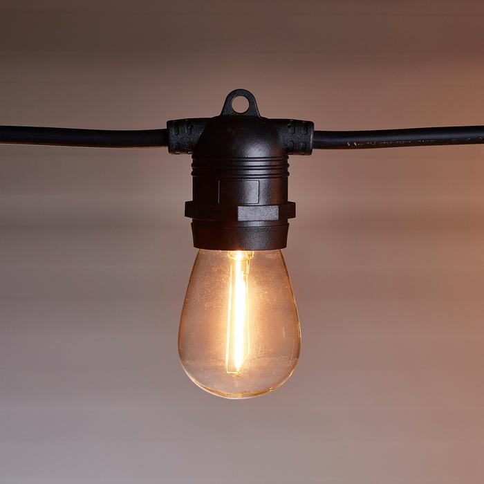 Nahaufnahme einer warmweiß leuchtenden Glühbirne an schwarzem Kabel